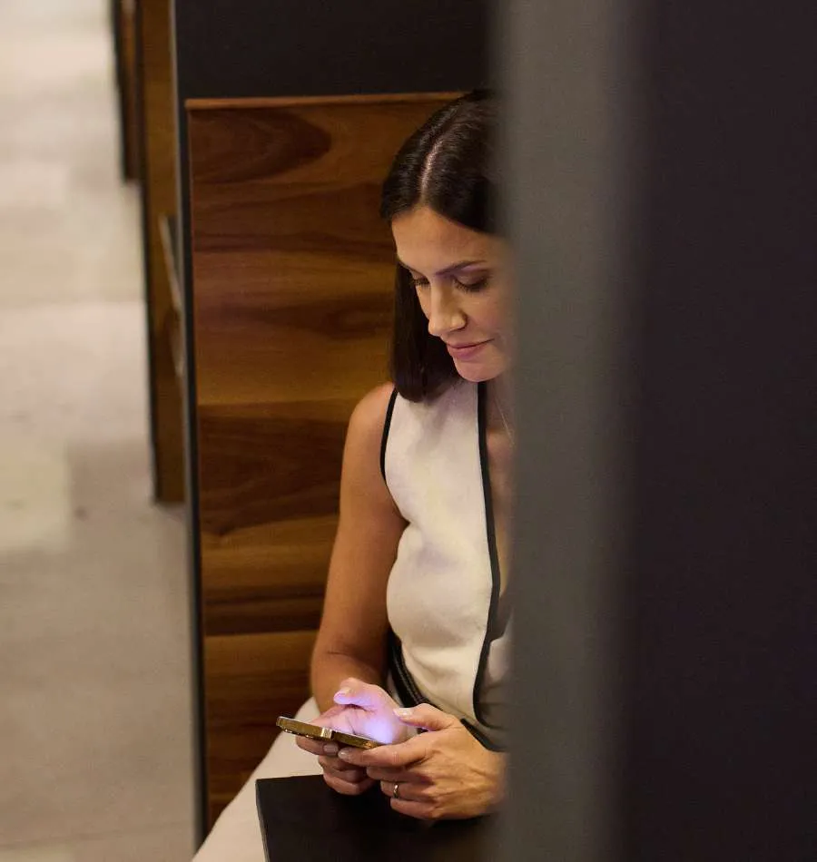Woman with dark hair sitting and using a smartphone, partially obscured by a vertical dark object.